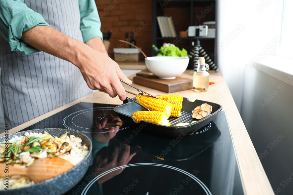 Young man frying tasty corn in kitchen, closeup