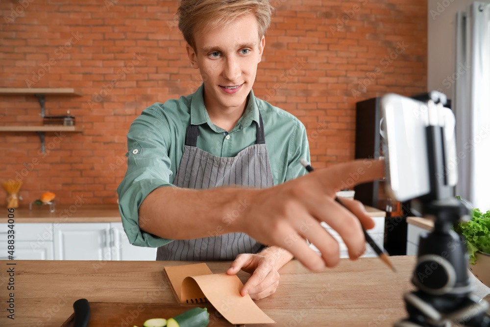Young man with notebook using mobile phone in kitchen
