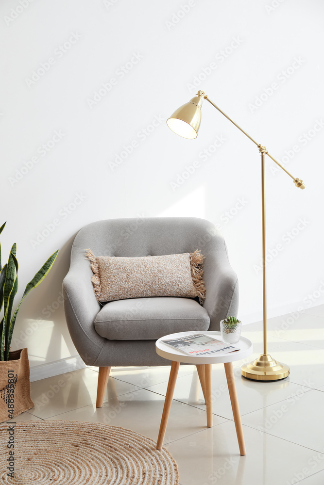Golden standing lamp, armchair and table near light wall