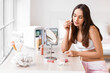 © Pixel-Shot - Beautiful young woman applying makeup at dressing table at home