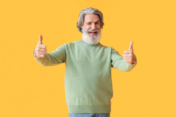 Sticker - Handsome senior man in knitted sweater showing thumb-up on yellow background