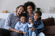© fizkes - Portrait of happy bonding African American family showing keys to camera, sitting on couch, Joyful adorable small children and caring young multiracial couple parents celebrating moving into own home.