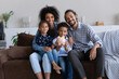 © fizkes - Portrait of loving African American family sitting on couch with piggybank in hands. Caring young joyful couple parents teaching little kids saving money for future, financial literacy for children.