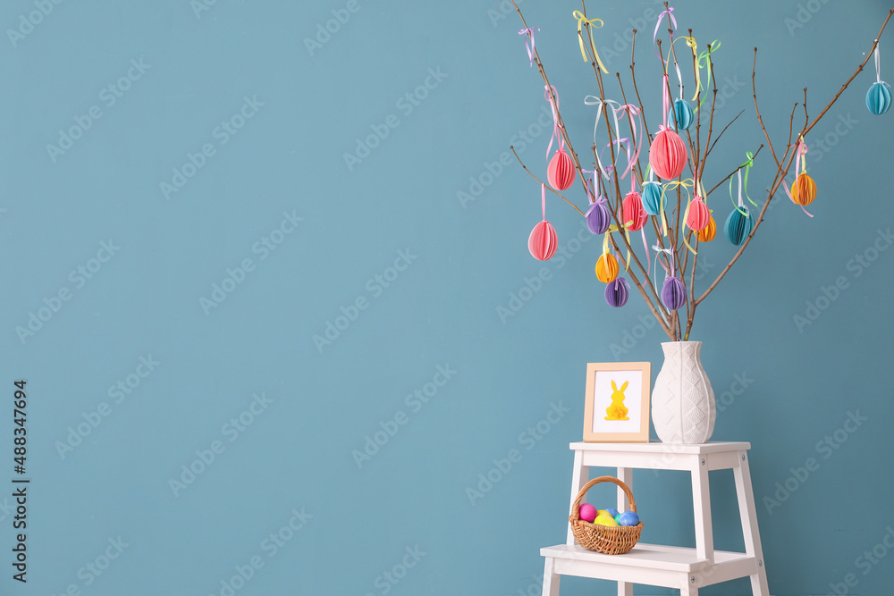 Basket with Easter eggs, photo frame and vase with tree branches near color wall