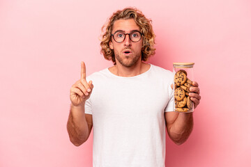 Wall Mural - Young caucasian man holding cookies jar isolated on pink background having some great idea, concept of creativity.