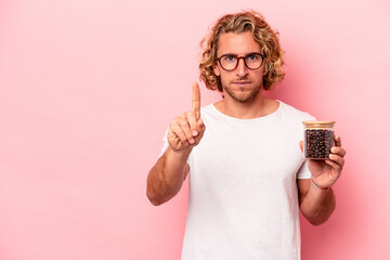 Wall Mural - Young caucasian man holding coffee jar isolated on pink background showing number one with finger.