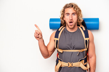 Wall Mural - Young mountaineer caucasian man with a big backpack isolated on white background pointing to the side