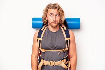 Wall Mural - Young mountaineer caucasian man with a big backpack isolated on white background confused, feels doubtful and unsure.