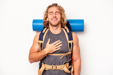 Wall Mural - Young mountaineer caucasian man with a big backpack isolated on white background laughs out loudly keeping hand on chest.