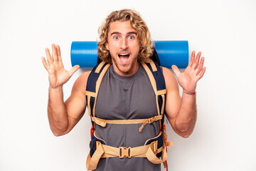 Wall Mural - Young mountaineer caucasian man with a big backpack isolated on white background receiving a pleasant surprise, excited and raising hands.