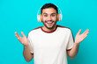 © luismolinero - Young Brazilian man isolated on blue background surprised and listening music