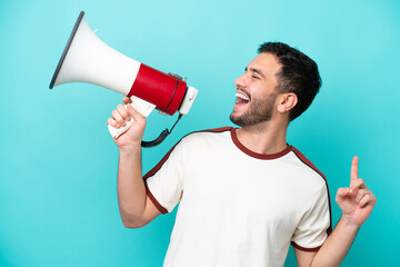 Wall Mural - Young Brazilian man isolated on blue background shouting through a megaphone to announce something in lateral position