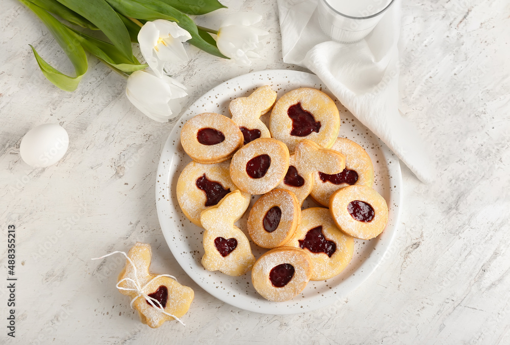Plate with delicious Easter cookies and tulip flowers on light background