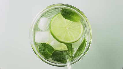 Wall Mural - Soda water with lime, mint, ice and drinking straw in the glass on the white background, rotate, top view, 4k. Fresh lime detox water with bubbles.