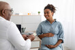 Mature experienced black doctor showing pills to pregnant lady