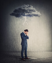 Pessimistic And Depressed Businessman Standing Under Rain As The Negative Thoughts Stands Over His Head Like A Storm Cloud. Person Suffering Anxiety And Headache. Concept For Emotional Crisis