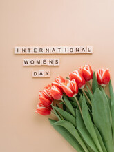 International Women's Day Or Eight March Concept With Copy Space. International Women's Day Text And Bunch Of Red Tulip On Beige Champagne Background. Top View Or Flat Lay. Vertical