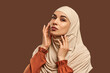 Portrait of beautiful modern muslim woman with natural make-up dressed in beige hijab posing on brown background in studio. Facial skin care, female beauty.
