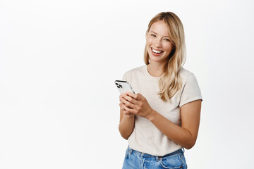 Cellular technology, mobile apps concept. Smiling beautiful woman using smartphone, looking at her phone with happy face, reading, standing over white background