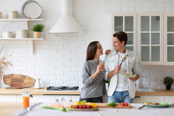 Beautiful young couple looks at each other and smiles while eating in the kitchen. Healthy eating