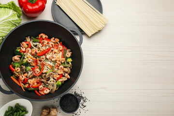 Stir fried noodles with mushrooms, shrimps and vegetables in wok on white wooden table, flat lay.  Space for text