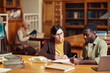 © Seventyfour - Portrait of female professor tutoring black student in classic library interior at college