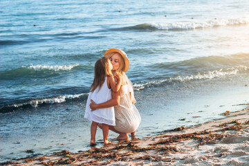 A mother with a child in motion throws up a girl on the seashore in a straw hat, happy emotions