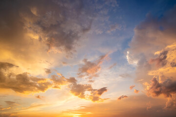 dramatic moody sunset landscape with puffy clouds lit by yellow setting sun and blue sky