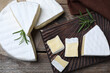 Tasty cut brie cheese with rosemary on wooden table, flat lay
