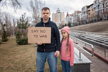 Middle aged father with his daughter holding a poster with anti-war message over cityscape background. Protest against the Russian intervention to Ukraine, activism and human rights movement