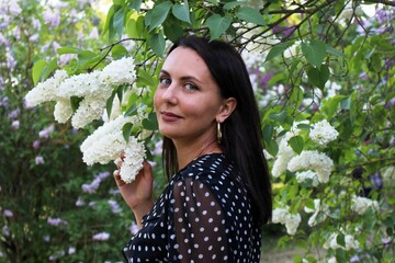 A beautiful girl of model appearance in a summer dress in a blooming garden among the aromas of bright lilac on a summer day.