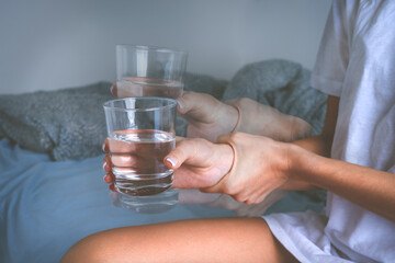 Woman holding glass of water in shaky hands and suffering from Parkinson's disease symptoms or essential tremor.