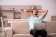 © Elnur - Young man sitting on the sofa with computer at home