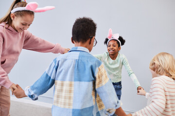 Diverse group of children wearing bunny ears and holding hands while celebrating Easter together