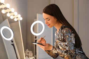 Wall Mural - Young woman applying make up near illuminated mirror indoors