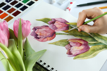 Canvas Print - Woman painting tulips in sketchbook at white table, closeup