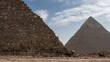 The two great pyramids of Giza- Cheops and Chephren against the blue sky. The ancient masonry walls are visible. At the foot are horses harnessed to carts. Egypt