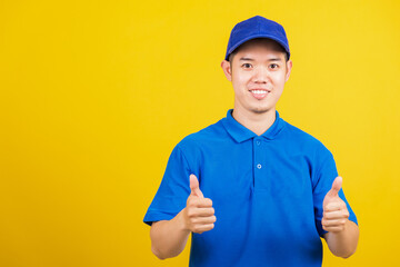 Wall Mural - Portrait professional attractive delivery happy man standing he smile wearing blue t-shirt and cap uniform showing thumb up gesture looking to camera, studio shot isolated on yellow background