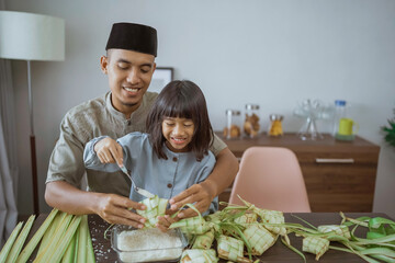 father and daughter making ketupat together at home