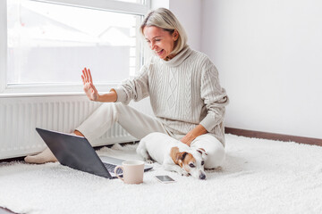 Wall Mural - Happy middle aged woman with dog using her laptop at cozy white home