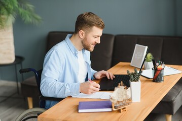 Wall Mural - Disabled person in the wheelchair works in the office at the computer. He is smiling and passionate about the workflow.