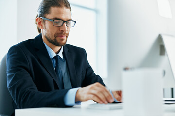 Wall Mural - a man in a suit with glasses typing at his desk