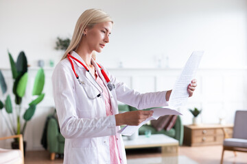 Female doctor stands in office and reads medical documents