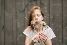Cute Girl Blowing Dandelions By Wall