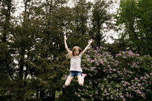 Cheerful Girl Jumping In Front Of Lilac Flowers In Nature