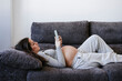 © Westend61 - Pregnant woman using smart phone lying on sofa at home