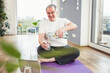 © Westend61 - Happy senior man sitting on exercise mat pouring water in drinking glass at home