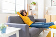 © Westend61 - Young woman with hands behind head relaxing on sofa in living room
