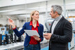 © Westend61 - Smiling woman with tablet PC discussing ideas with colleague in factory