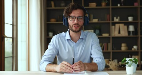 smiling confident millennial male teacher in headset sit at office desk give remote video lecture ta